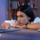 A forlorn young woman slumped over a desk looking at a laptop