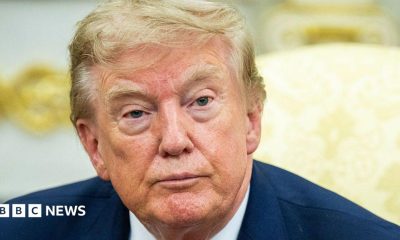 Donald Trump in a navy suit with a yellow background.