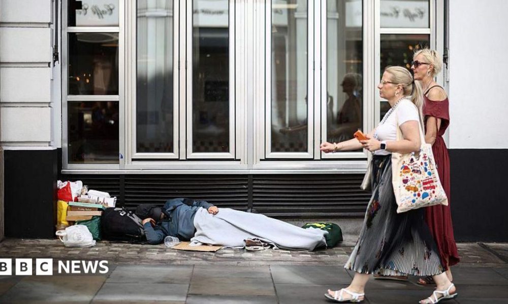 Two women walk past a person lying on the pavement in London, 28 July