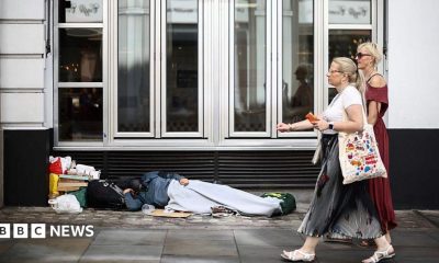 Two women walk past a person lying on the pavement in London, 28 July