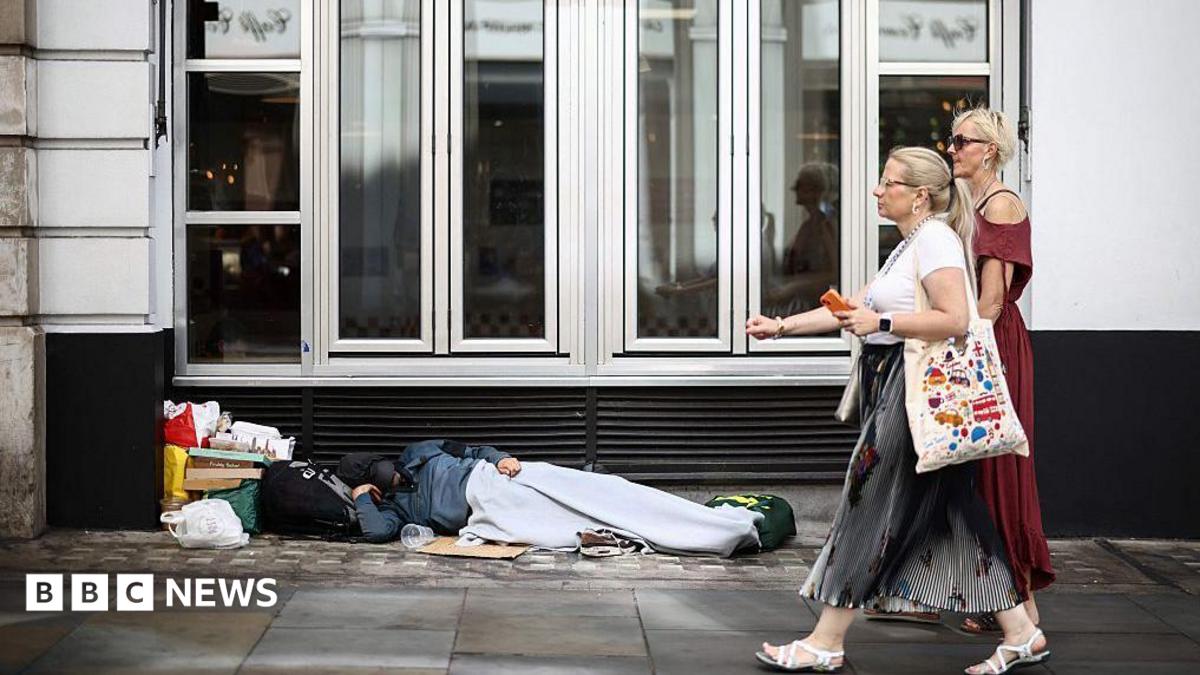 Two women walk past a person lying on the pavement in London, 28 July