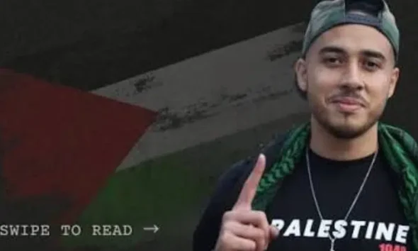 Ahmad Hajahmad Jarrar, a pro-Palestine activist, smiles with his index finger pointing up in a baseball cap turned backwards and a scarf draped on his shoulders. His jumper has 'Palestine' printed on it