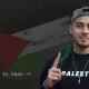Ahmad Hajahmad Jarrar, a pro-Palestine activist, smiles with his index finger pointing up in a baseball cap turned backwards and a scarf draped on his shoulders. His jumper has 'Palestine' printed on it