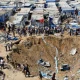 Palestinians inspect the site of an overnight Israeli strike on a medicine warehouse next to tents sheltering displaced families in Deir el-Balah, in central Gaza, on 1 August 2026. There is a huge crater in the earth.