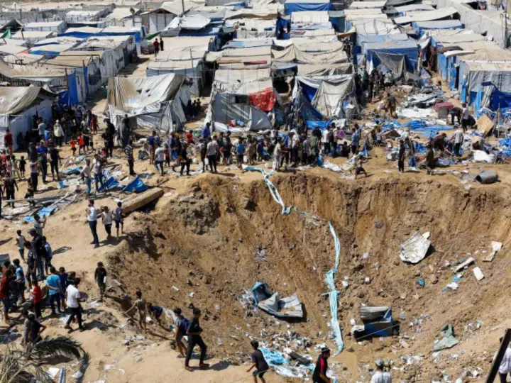 Palestinians inspect the site of an overnight Israeli strike on a medicine warehouse next to tents sheltering displaced families in Deir el-Balah, in central Gaza, on 1 August 2026. There is a huge crater in the earth.