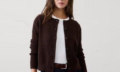 A woman wearing a white top, dark blue jeans, and a dark brown cardigan