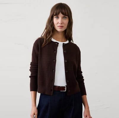 A woman wearing a white top, dark blue jeans, and a dark brown cardigan