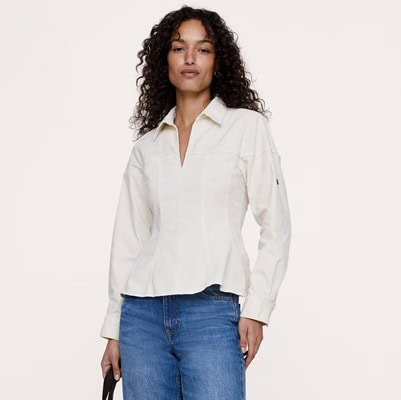 A woman wearing a beige button-front blouse and medium blue jeans