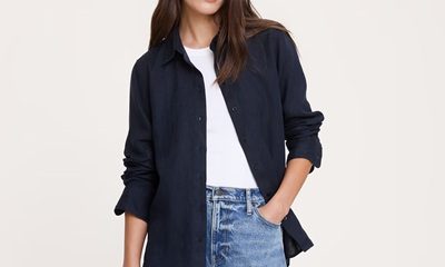 A woman wearing a white top, navy button-front shirt (open), and light blue jeans