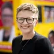 New Greater Manchester mayor, Bev Craig, smiling with her signature cropped hair and round-rimmed glasses in front of a campaign bus