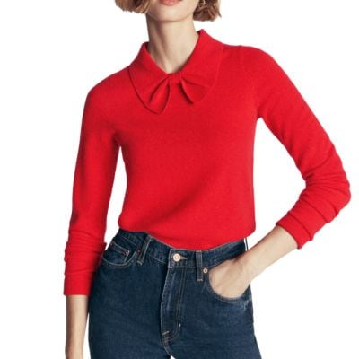 A woman wearing a red bow-neck sweater and dark blue jeans