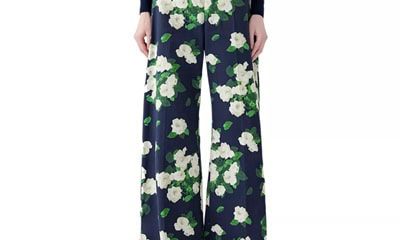 A woman wearing a navy, green, and white floral pant and gold shoes, plus a navy top with a couple of white flowers