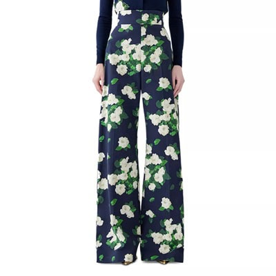 A woman wearing a navy, green, and white floral pant and gold shoes, plus a navy top with a couple of white flowers