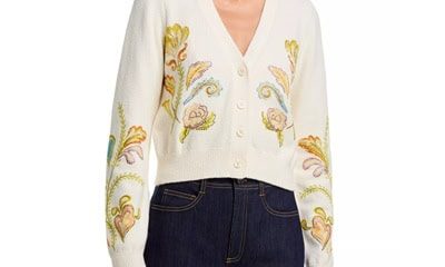 A woman wearing dark blue jeans and an ivory cardigan with floral embellishments