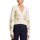 A woman wearing dark blue jeans and an ivory cardigan with floral embellishments