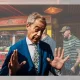 Nigel Farage, leader of Reform UK, reacts to a question from journalists in Clacton and he's captured with both hands up, palms facing outwards. An amusement park games machine is behind him.