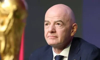 FIFA president Gianni Infantino with a neutral expression in suit and tie and in the foreground is a partially shown and blurred golden World Cup trophy