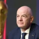 FIFA president Gianni Infantino with a neutral expression in suit and tie and in the foreground is a partially shown and blurred golden World Cup trophy