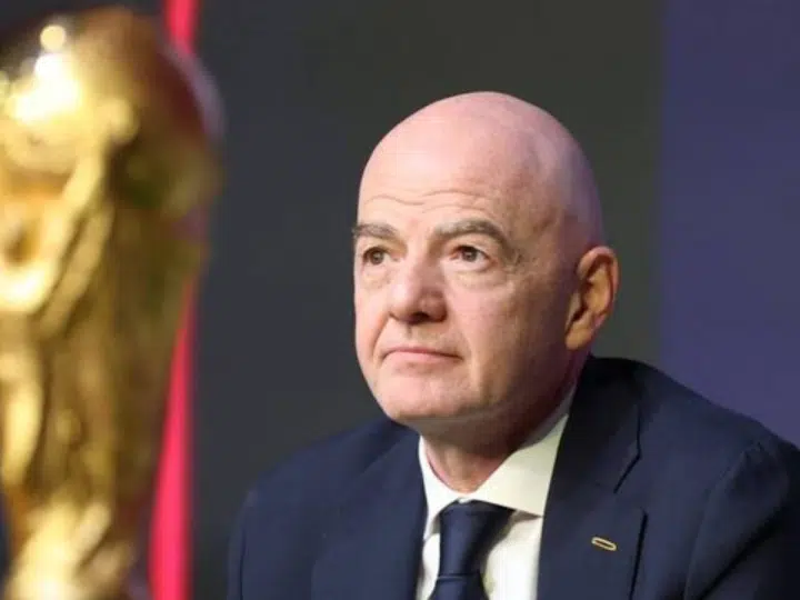 FIFA president Gianni Infantino with a neutral expression in suit and tie and in the foreground is a partially shown and blurred golden World Cup trophy
