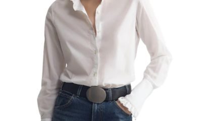 A woman wearing a white button-front blouse and blue jeans with a black belt with large belt buckle