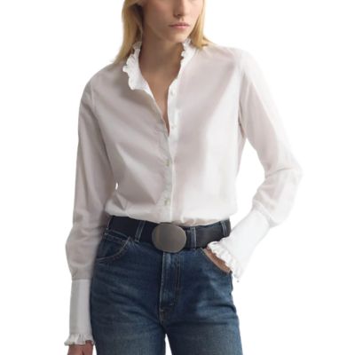 A woman wearing a white button-front blouse and blue jeans with a black belt with large belt buckle