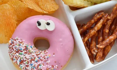 Illustrative image of unhealthy school lunch including a doughnut, chips, crisps and twiglets. School lunch menus.