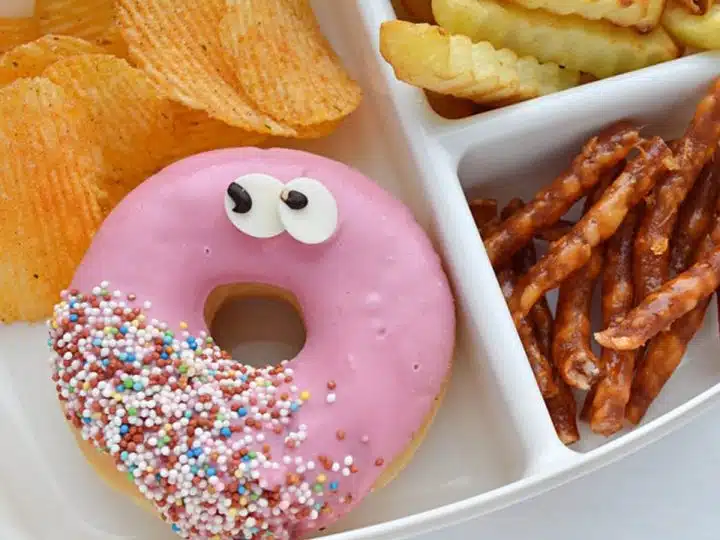 Illustrative image of unhealthy school lunch including a doughnut, chips, crisps and twiglets. School lunch menus.