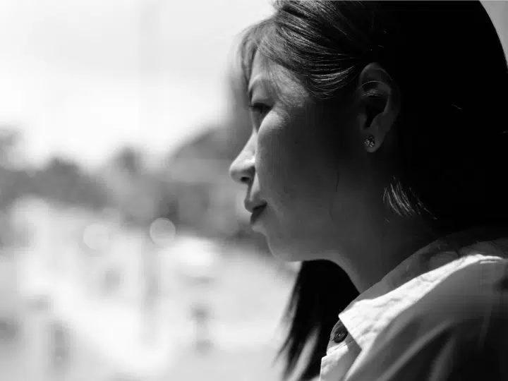 A black and white portrait of a woman gazing out of a window, capturing reflection and contemplation, in relation to the autism strategy story