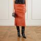 A woman (torso cropped out) wearing a black top, brown leather skirt, and black tall boots. She is carrying a black handbag..