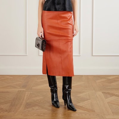A woman (torso cropped out) wearing a black top, brown leather skirt, and black tall boots. She is carrying a black handbag..