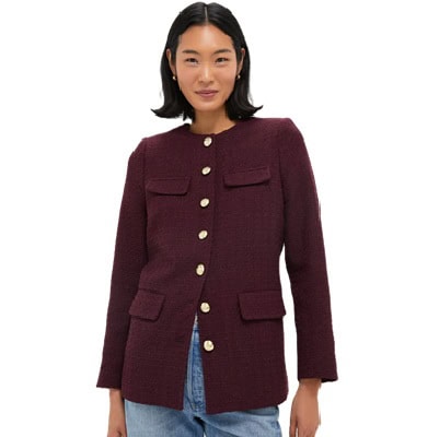 A woman wearing a wine-colored jacket with gold buttons, and light blue jeans