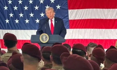 President Donald Trump speaks to beret-wearing US military soldiers infront of a large American flag at Fort Bragg, North Carolina on Friday, 13 February 2026