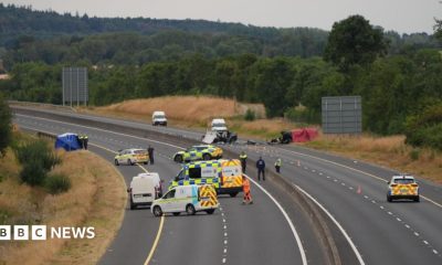 A wide shot of a car crash site. Many emergency service vehicles are on the road and debris from the crash.