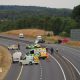 A wide shot of a car crash site. Many emergency service vehicles are on the road and debris from the crash.