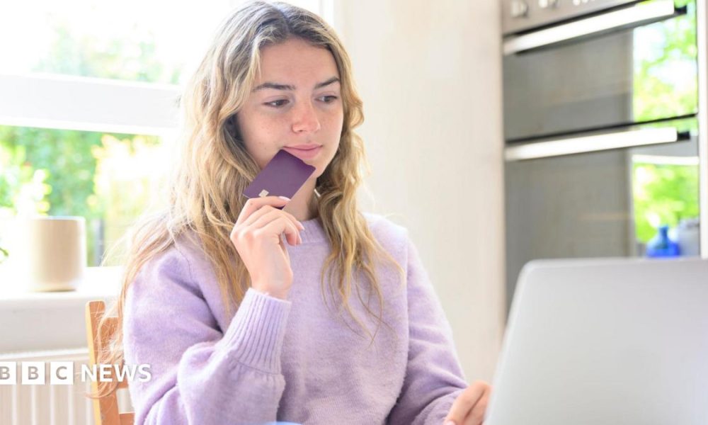 A young woman sitting at her laptop while holding a credit card