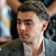 Luigi Mangione is seen from the shoulders up, sitting at the defence table in court. He wears a charcoal grey suit.
