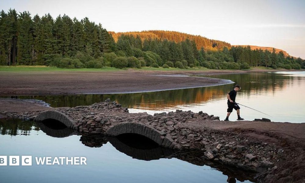 View of a depleted reservoir with a boy walking across a bridge with a fishing rod