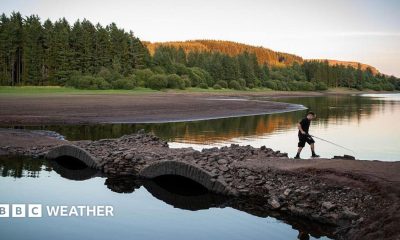 View of a depleted reservoir with a boy walking across a bridge with a fishing rod