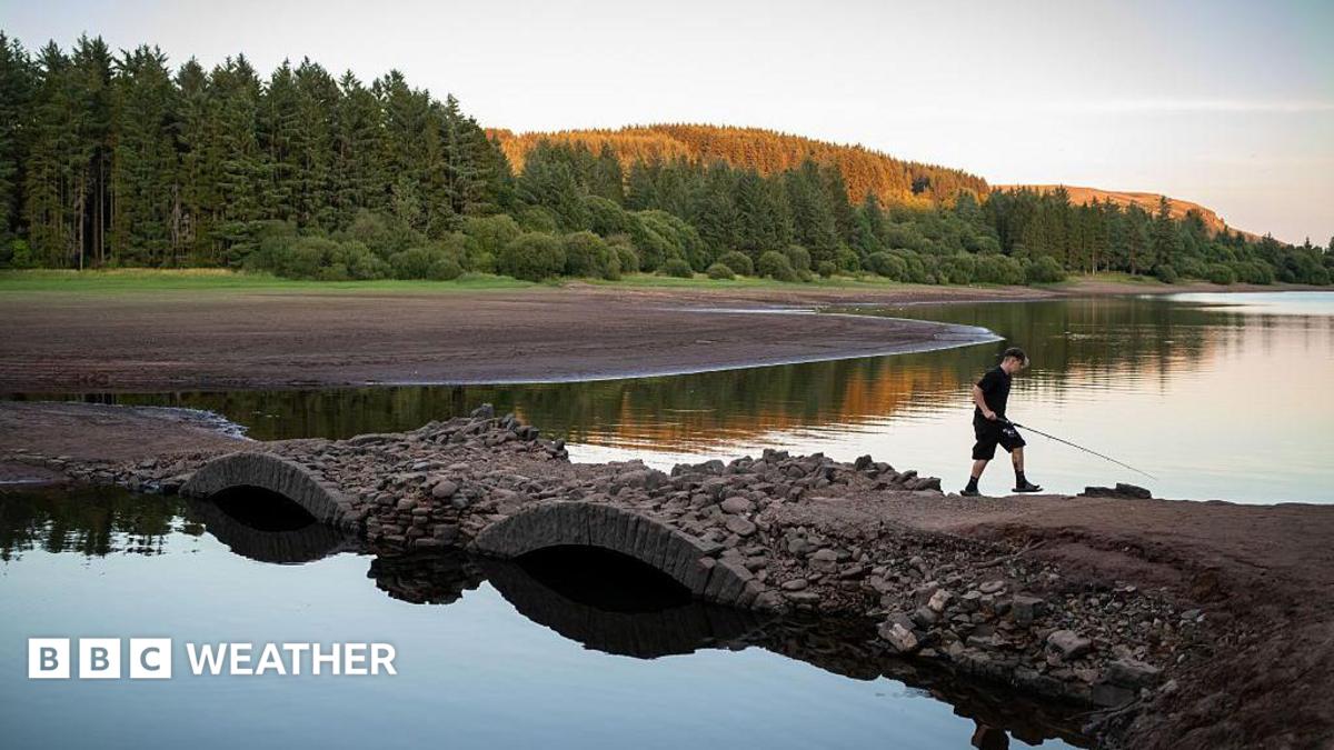 View of a depleted reservoir with a boy walking across a bridge with a fishing rod