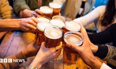 A young group of friends clinking pint glasses of beer together around a pub table