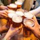 A young group of friends clinking pint glasses of beer together around a pub table