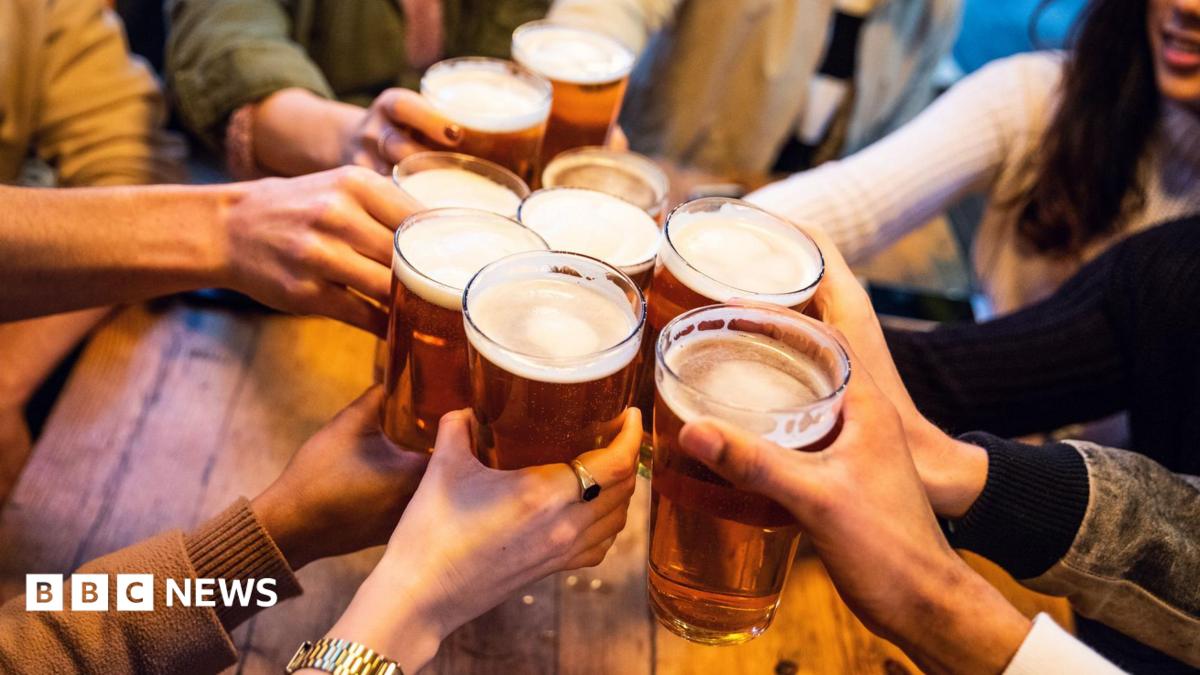 A young group of friends clinking pint glasses of beer together around a pub table