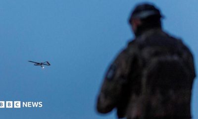 A Ukrainian soldier operating a drone, which is flying in the air in the background