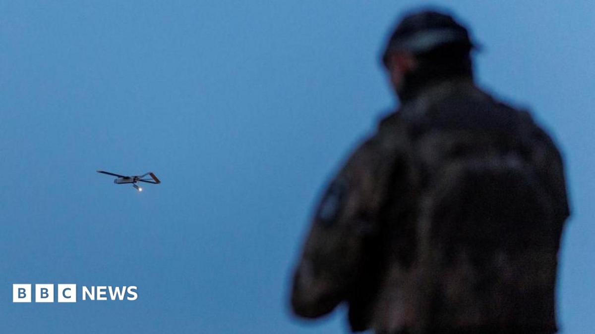 A Ukrainian soldier operating a drone, which is flying in the air in the background