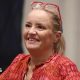 Lucy Davis, a fair-haired woman in a red top and with red-framed glasses worn on top of her head, is seen sitting down and smiling at the For The Love of Fantasy & Sci-Fi convention at Excel London on Saturday 22 August 2026