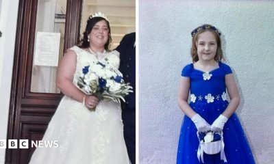 A composite image of Natalie McDonald and Valentina Foster. McDonald is wearing a white wedding dress with a tiara perched on her head. She has long dark hair and is holding a bouquet of white roses with four blue ones dotted within it. Valentina wears an electric blue dress with white flowers on the neckline and waist. She has long light brown hair with a blue and white headband. She is holding a small white basket with white and blue roses and she wears white gloves.
