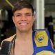 A man with dark hair smiling with a boxing belt over his shoulder.
