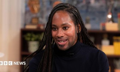 Jason Arday pictured during a TV interview in March 2023. He wears a black turtle-neck top.