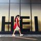 A woman in a red dress looks at her smartphone while walking past a Shein sign outside the company's office in Guangzhou, China.