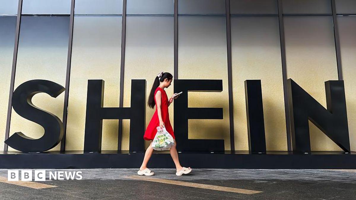 A woman in a red dress looks at her smartphone while walking past a Shein sign outside the company's office in Guangzhou, China.